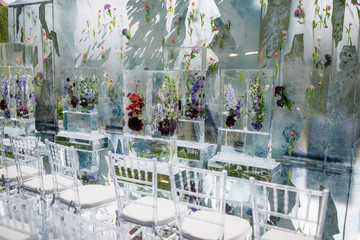 Ice cubes with violet flowers inside  stand before transparent plastic chairs