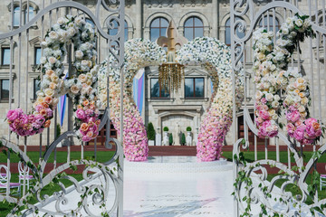 Wedding altar made of archs of pink, yellow and white flowers stands on the backyard