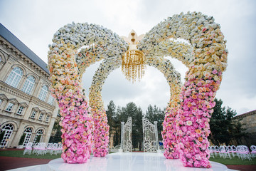 Wedding altar made of archs of pink, yellow and white flowers stands on the backyard