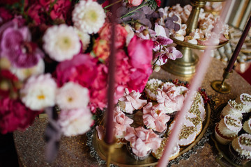 Candy bar decorated with pink flowers and sweets served on golden dishes