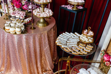 Golden dishes with eclairs, cookies, macaroons and cupcakes stand on pink candybar