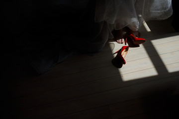 Red shoes lie before bride on the floor