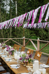 Dinner table served with candles and violet lilac stands on wooden porch
