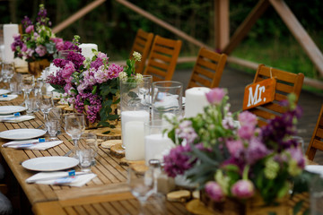 Fototapeta na wymiar Dinner table served with candles and violet lilac stands on wooden porch