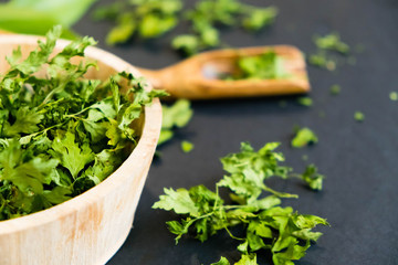 Dried cilantro leaves on a wooden spoon. Natural light. Selective focus. Close up on a black background. Top view, flat lay. copy space. dried grapes