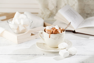 Mug of hot chocolate with marshmallows, on light wooden background with open book