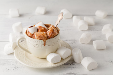 Mug of hot chocolate with marshmallows, on light wooden background