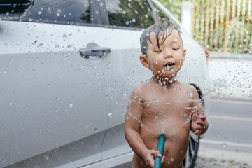 Happy asian little boy having fun to play with the water while washing the car in vintage color tone