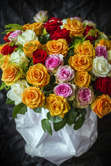 A beautiful and colorful bouquet of big roses in different colors in white paper with a black velvet background