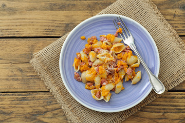 pasta italiana con zucca gialla e salsiccia su sfondo rustico