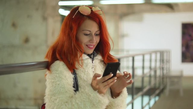 Beautiful red hair young woman with mobile and good mood at art gallery