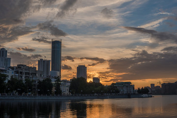 Fototapeta na wymiar Yekaterinburg city center on sunset. City pond view, amazing clouds and sky. High buildings, skyscrapers on the embankment of the river Iset