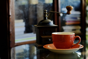 Red coffee mug placed in front of a coffee grinder on the table in a cafe.