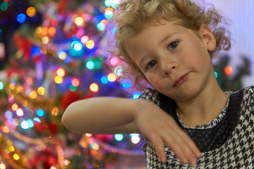 Mała dziewczynka pozuje do portretu na tle rozmytych światełek z drzewka bożonarodzeniowego.