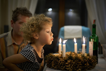 Mała dziewczynka zdmuchuje świeczki ze stroika bożonarodzeniowego.
