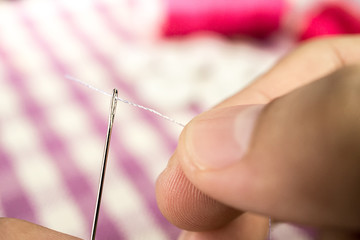hand holding white thread psuh through the hole of sewing needle
