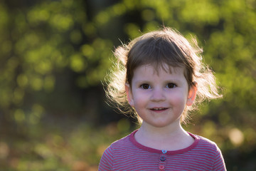 Portret małej dziewczynki w plenerze. Rozmyte tło jesiennych drzew.