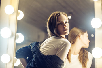 Sensual cute girl in blue jacket ready for romantic date. Adorable young woman posing near the makeup mirror in her room with sensual look.