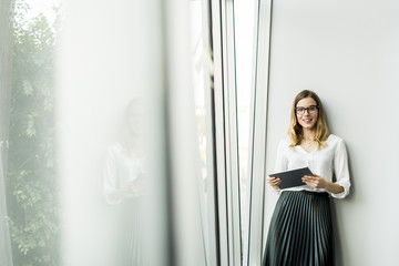 Young businesswoman standing wirth tablet in the office by window