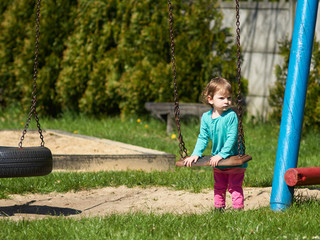 Dziewczynka bawi się jesienią na huśtawce na placu zabaw. 