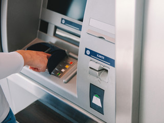 Side view of woman using ATM Automatic Teller Machine cash machine to enter the security PIN and retrieve withdrawal withdrawal money