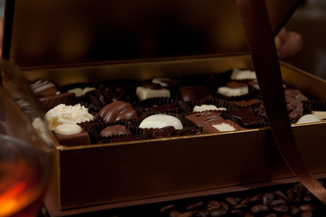 closeup of a chocolate box full of Belgian pralines and a glass of luxury cognac