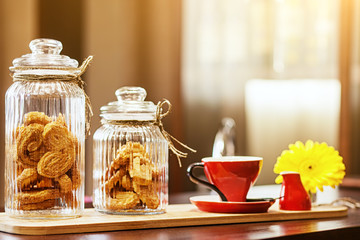 Still life of their red mug for coffee, glass jars with sugar cookies and chopped chrysanthemum on a brown table