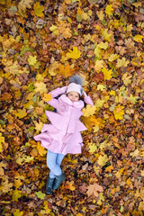 baby girl lying on autumn leaves in pink coat