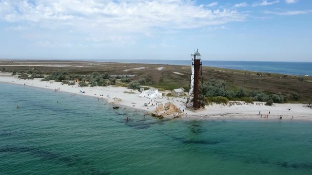 An awesome bird`s eye view of a white beacon and a black border tower on Dzharylhach island with wonderful seacoast covered with green wetland and sand in summer. The skyscape is fantastic