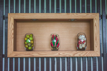 Vegetables (lemons, chilli, garlic) in glass jar on wooden shelf for kitchen decoration.