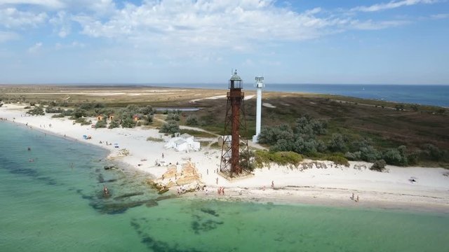 An exciting bird`s eye view of a border tower and a white lighthouse on Dzharylhach island with splendid seacoast covered with green wetland and sand in summer. The sky is blue and beautiful