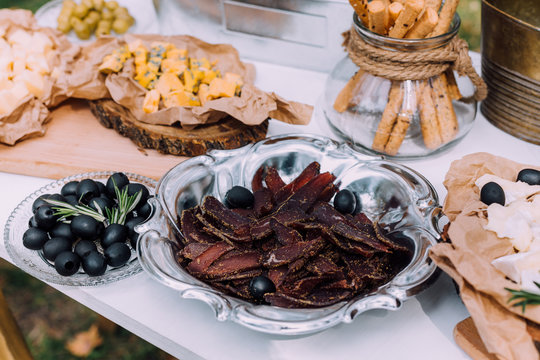 Salty and cheese bar of several kinds of cheese, grapes, olives and snacks decorated on vintage wooden table. Wedding or other holiday party outdoors