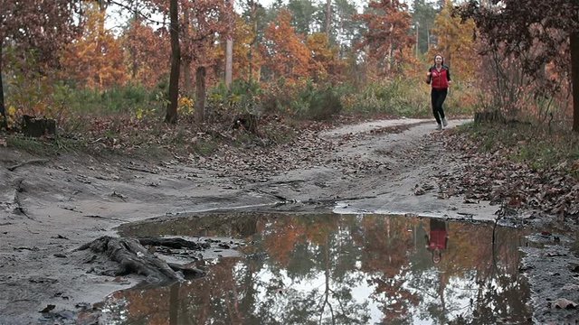 Doing sports. A woman runs along the road treading into a puddle.