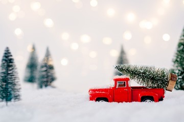 Red toy pickup car carrying Christmas tree - obrazy, fototapety, plakaty
