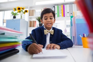 Smiling boy imitating as businessman writing on paper - obrazy, fototapety, plakaty