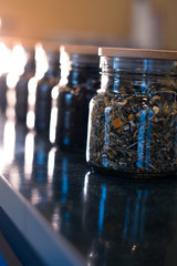 Different types of tea in glass jars on a blurred background.