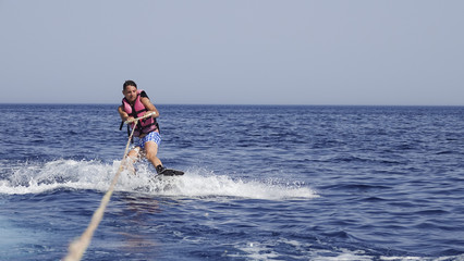 A man wakeboarder clings to a cable and moves behind a boat on the sea