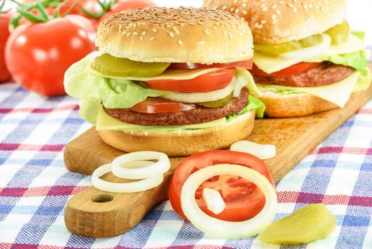 Concept image of traditional homemade hamburgers with beef, lettuce, cheese, tomato and pickles on wooden plank.