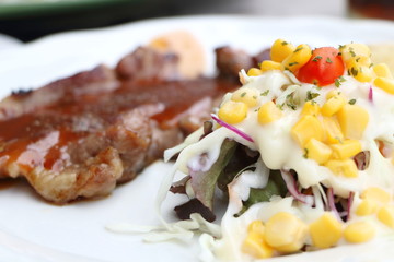 closeup focus salad vegetables with cream sauce and blur pork steak with sauce look delicious