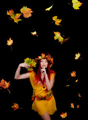 A beautiful young woman dresses up as an Autumn fairy   and wears a wreath on her head made out of Autumn leaves.  She poses for the camera while Autumn leaves fly around her.