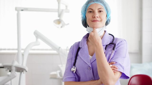 Portrait of confident professional female doctor standing in hospital room with arms crossed. Woman physician in medical mask and cap with stethoscope at work. Health care concept