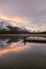 Naklejka na ściany i meble Woman Hiker Sitting on a Mountain Lake Dock at Sunrise on a Cold Morning