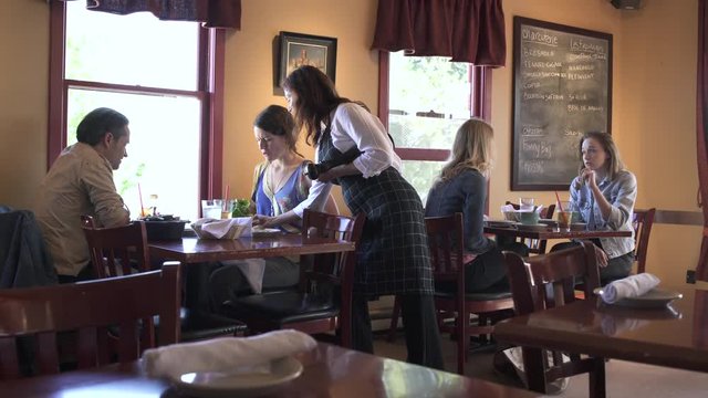 Panning shot of a waitress serving food for a couple