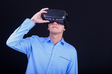 Young Asian man wearing virtual reality goggles with black background studio. Smartphone using with VR headset.