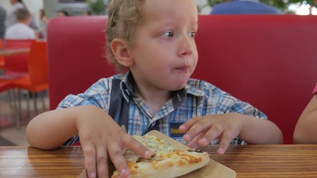 Closeup of cute little boy eating pizza in a cafe.