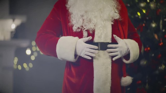Santa Claus pounding hands on belly on background New Year tree
