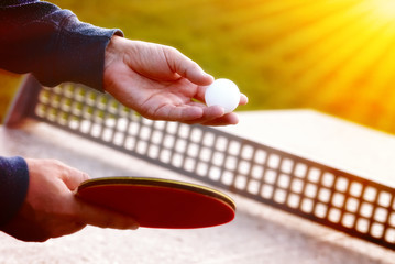 Close up of tennis player hands with tennis racket on nature background in sunny day.Closeup shot of a man serving in table tennis. Outdoor tennis table play
