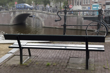 Bench on the edge of canal in Amsterdam, Netherlands. Bench, bicycle at railings, Amsterdam's canal and bridge on background