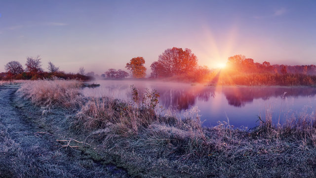 Sunrise on autumn frosty nature. Landscape of bright dawn over river. grass with hoarfrost shining on sun lights