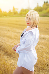 Fototapeta na wymiar Beautiful blond woman In white mens shirt posing In field. Sunny portrait.